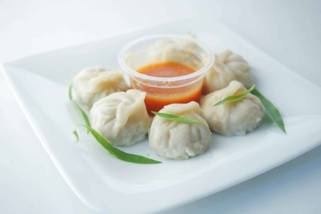 Steamed Nepali momos served with spicy tomato chutney on a white plate.